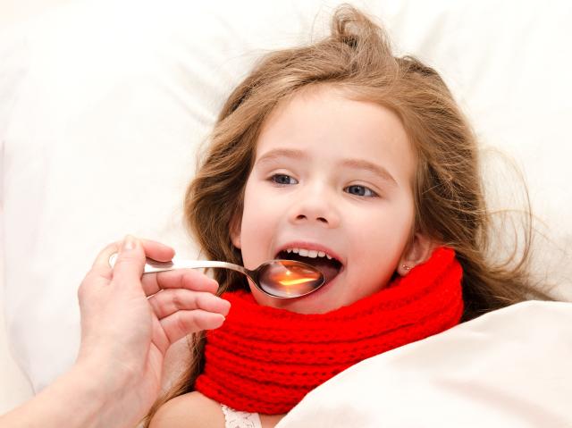 Niña enferma en cama tomando jarabe con cuchara