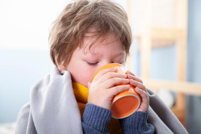 Niño enfermo con taza de caldo o infusión caliente