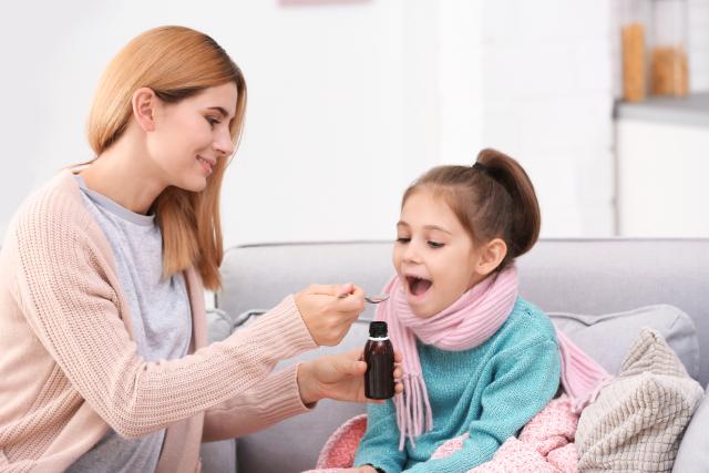 Madre dando jarabe con cuchara a niña enferma