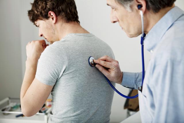 Médico auscultando hombre joven con tos