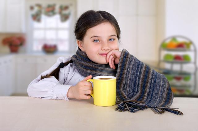Niña bebiendo té caliente en mesa cocina